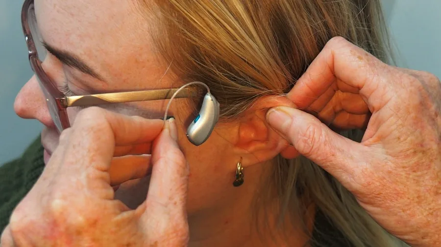 Close-up of a person carefully adjusting their hearing aid behind the ear for comfort and proper fit.