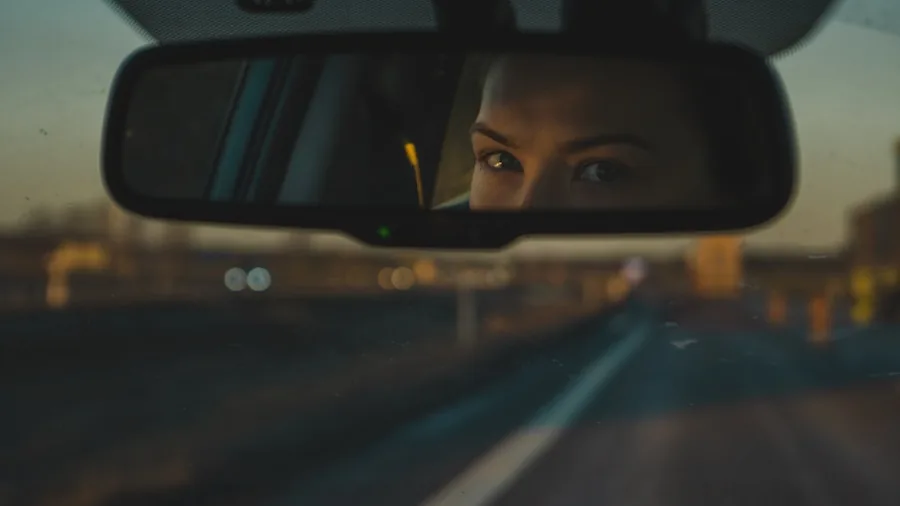 Driver looking in rear view mirror while reversing car, demonstrating vehicle safety awareness
