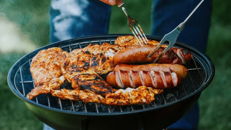 Family gathering around gas grill in backyard during outdoor dinner preparation