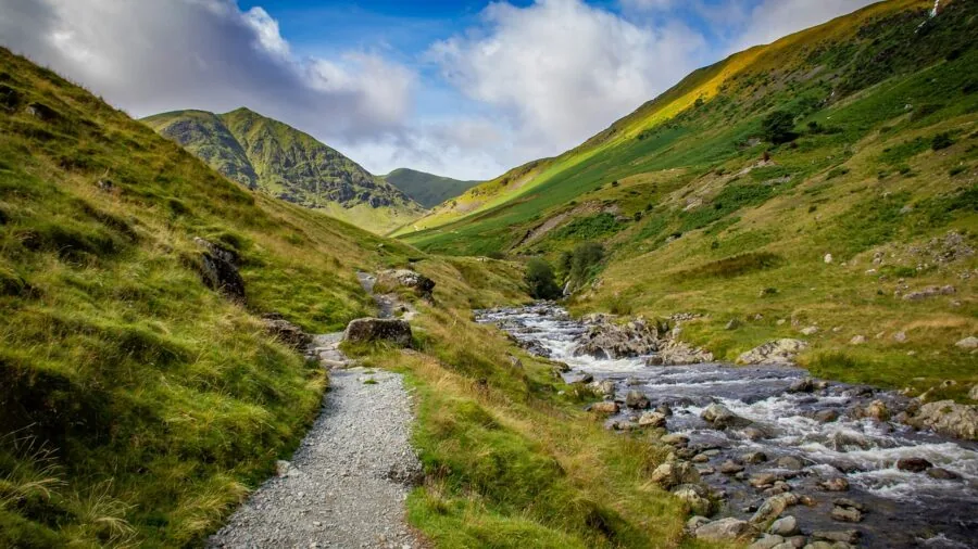 Female hiker crossing shallow stream on muddy forest trail during wet weather conditions
