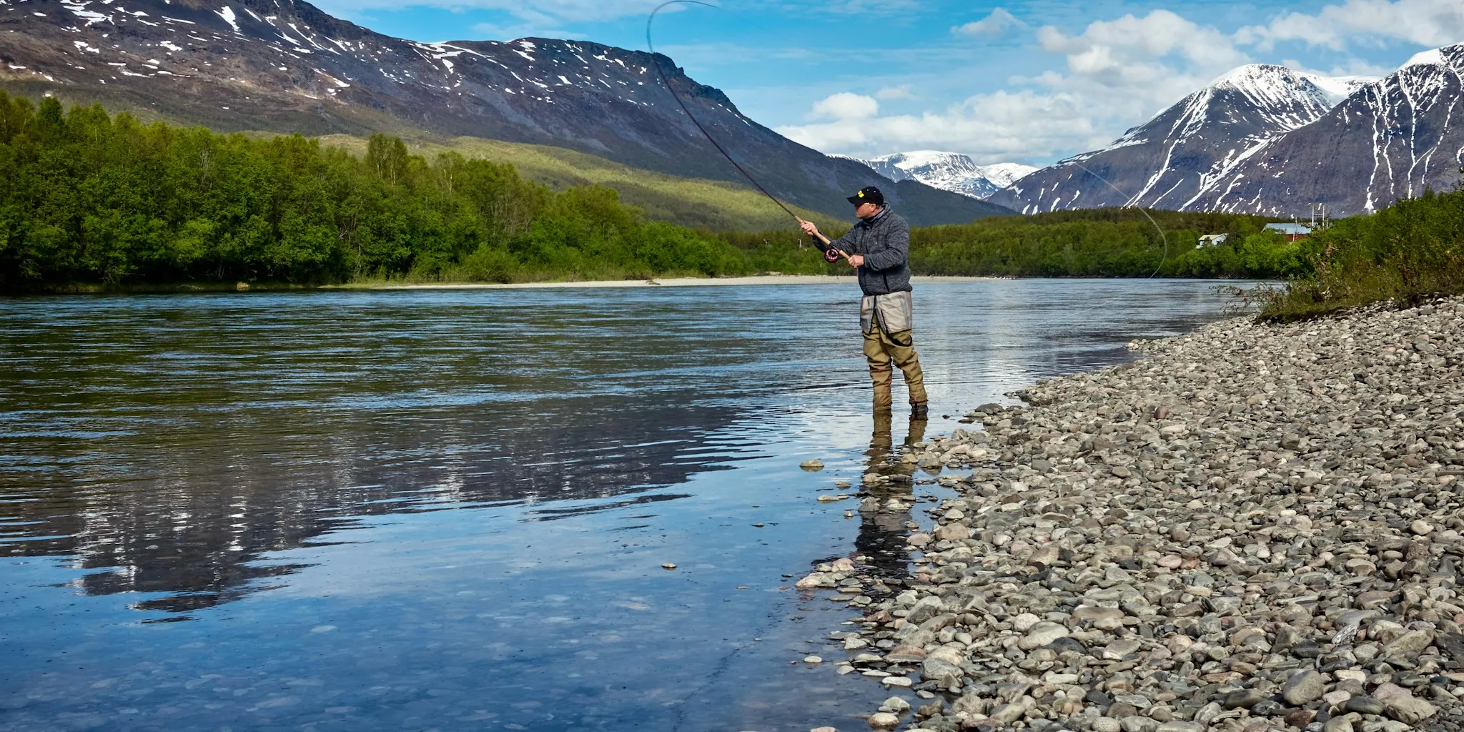 Fisherman casting line in peaceful trout stream with natural landscape