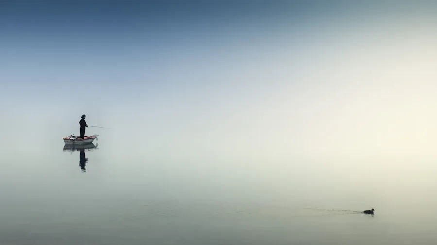 Fisherman casting line on peaceful water during early morning light with mist