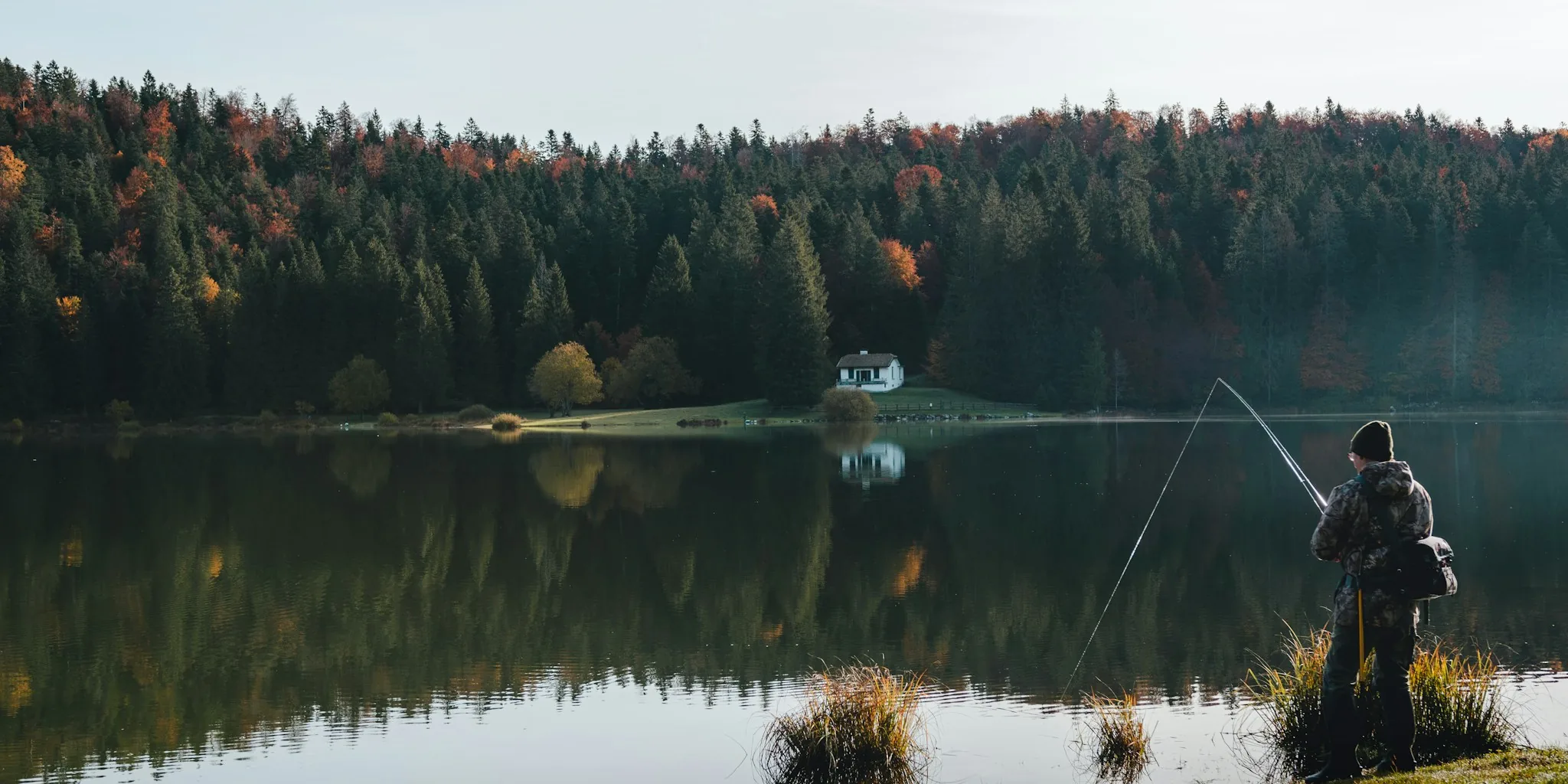 Fisherman casting rod on serene lake at sunrise with bass fishing lures
