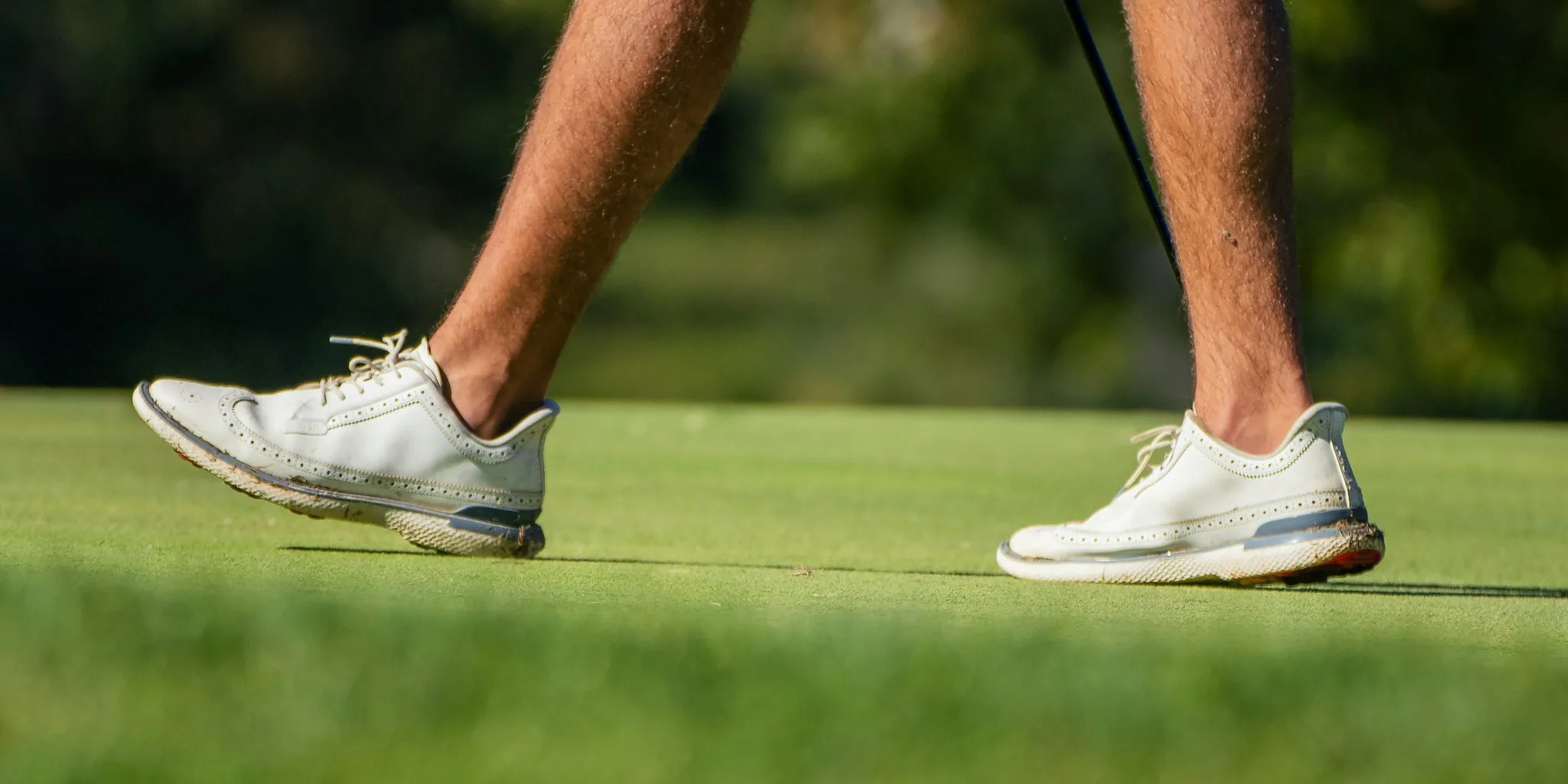 Golfer walking across green fairway wearing golf shoes during round of golf