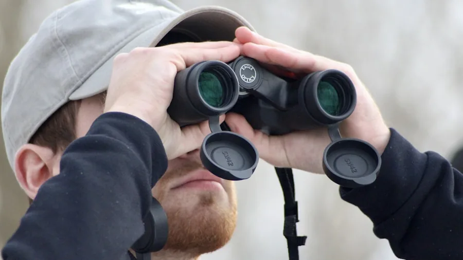 The %product_count% Best Hunting Binoculars 3 Hunter in weathered outdoor gear examining binoculars during rainfall in natural landscape