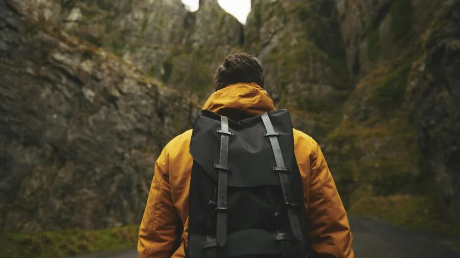 Man hiking through forest with backpack, demonstrating real-world wear on outdoor gear and clothing