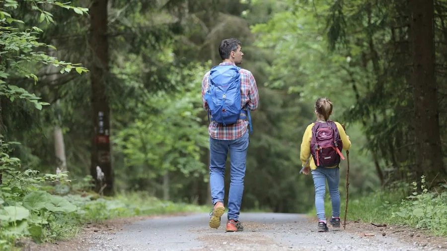 Parent wearing neutral-colored backpack while walking outdoors with child, depicting modern gender-neutral parenting style