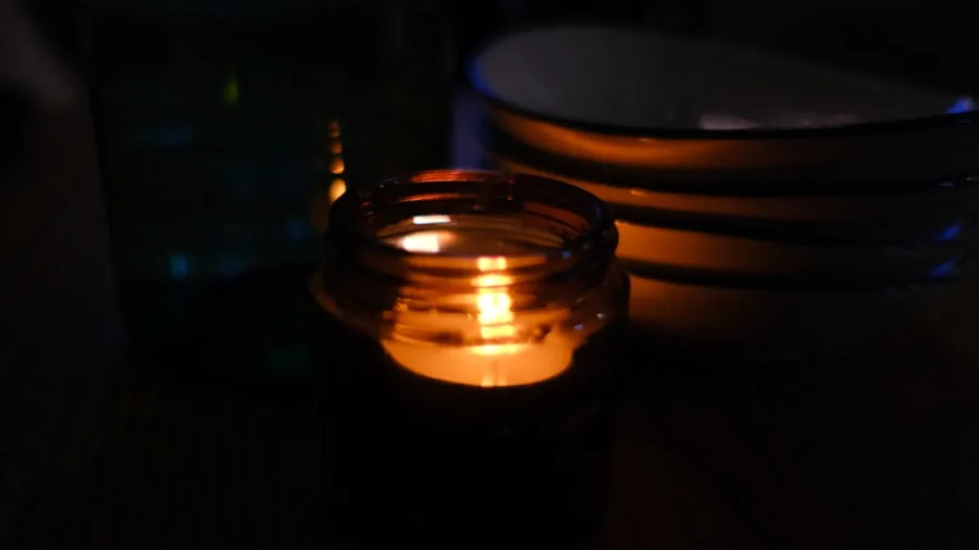 Person carefully lighting a scented candle in a cozy home setting with warm ambient lighting