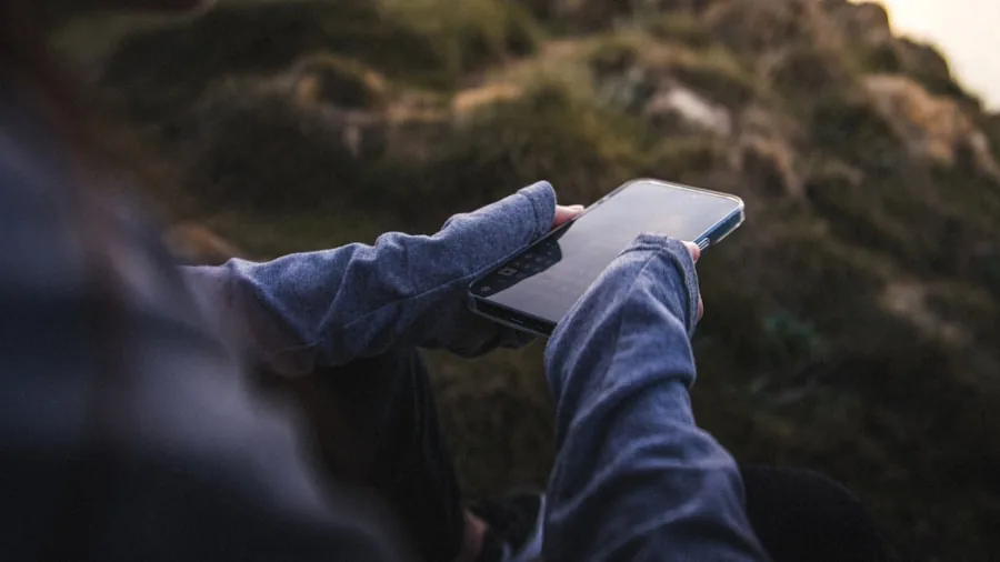 Person checking phone battery level while sitting outdoors in natural daylight