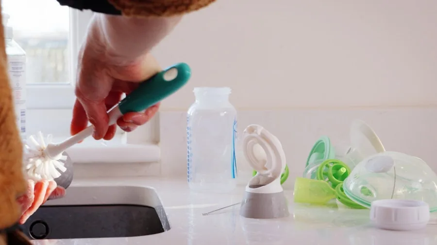 Person cleaning a reusable water bottle with a brush under running water at a kitchen sink