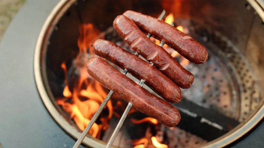 Person cooking food on cast iron skillet over open campfire flames outdoors