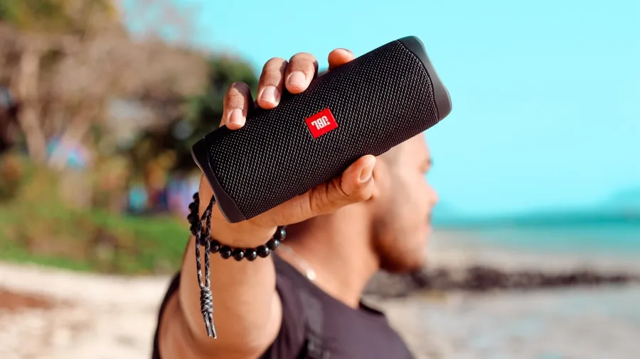 Person enjoying portable speaker at beach during sunny day with water and sand visible