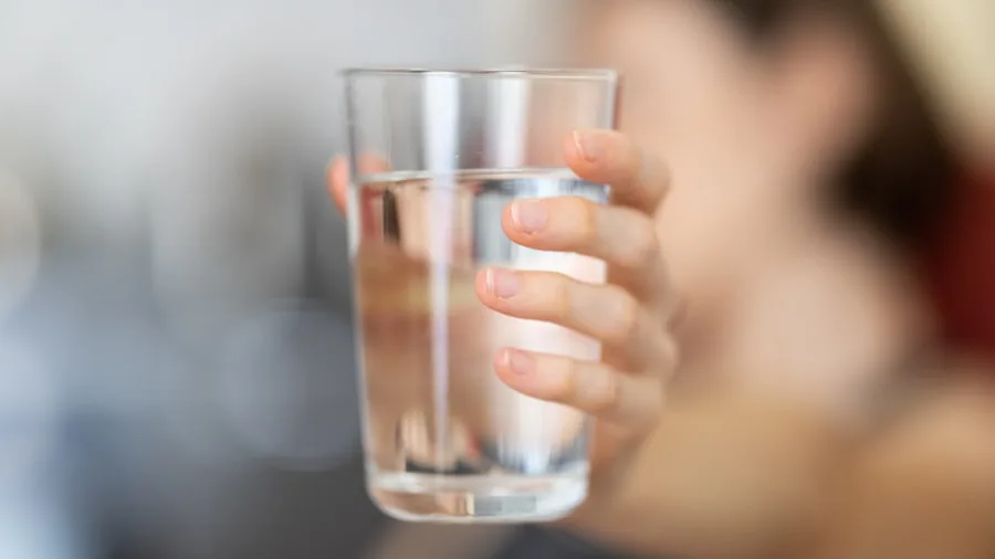 The 12 Best Under-Sink Water Filters 4 Person examining clean drinking water from kitchen tap, testing water quality at home sink