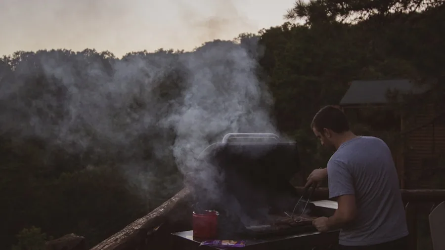 Person grilling food on backyard gas grill during twilight hours with illuminated controls