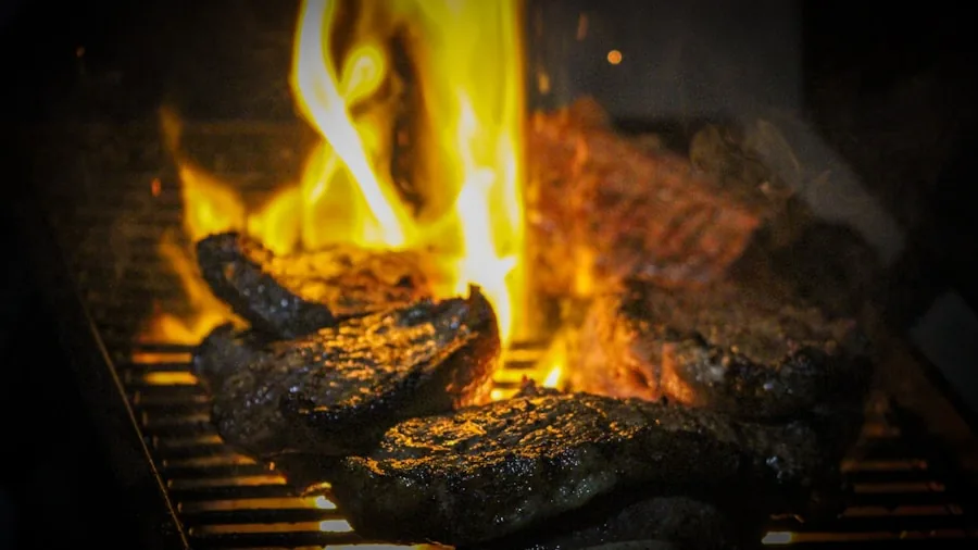 Person grilling steaks on outdoor grill with sear marks in backyard setting