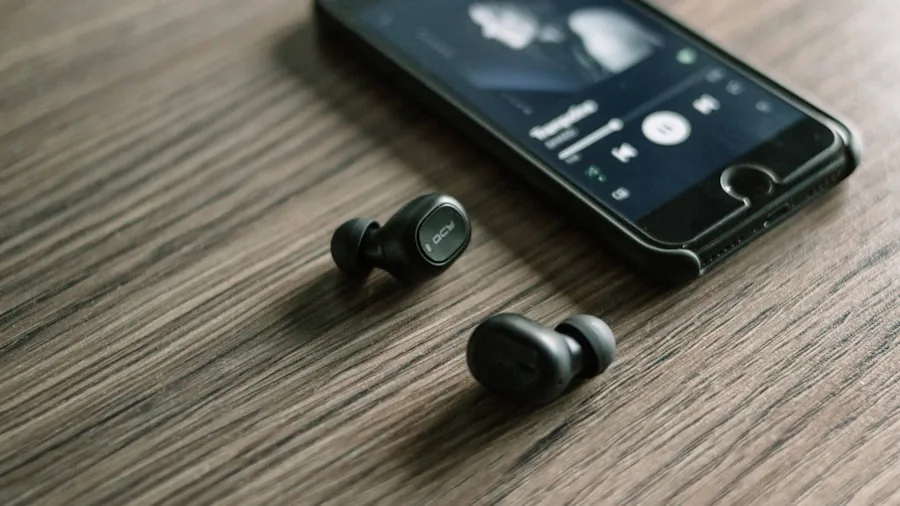 Person holding smartphone while wearing wireless earbuds, checking device compatibility and features