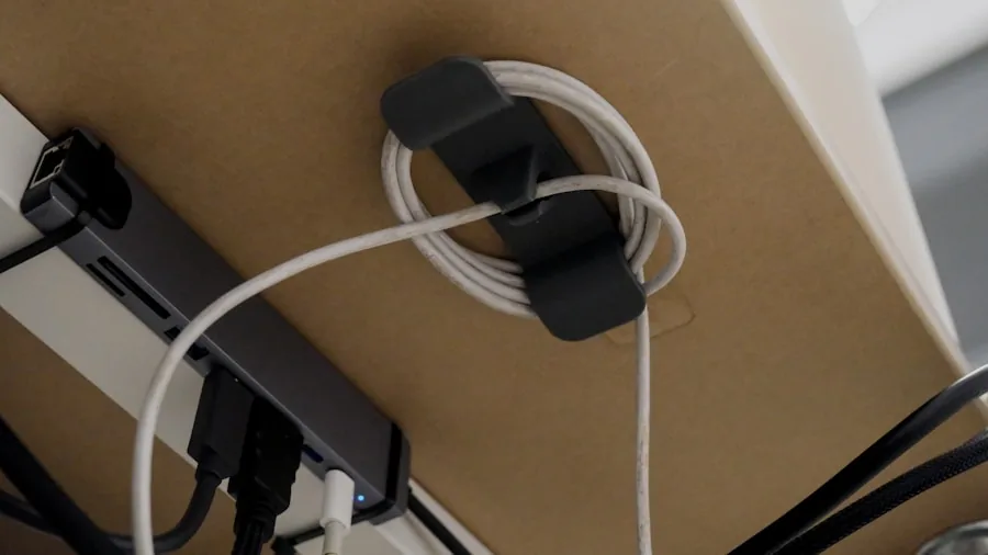 Person organizing charging cables at a home desk workspace with natural lighting