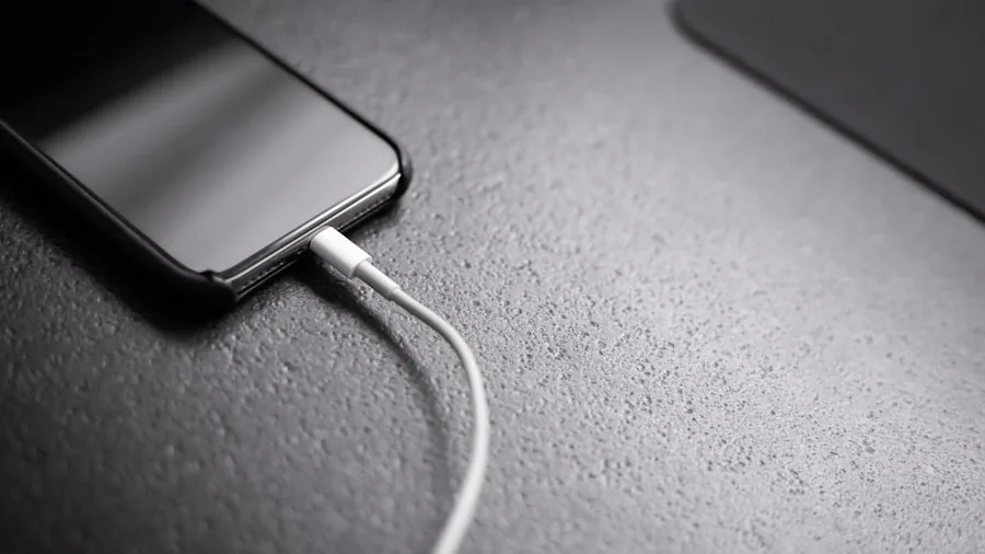 Person plugging smartphone into USB port on computer desk setup for charging