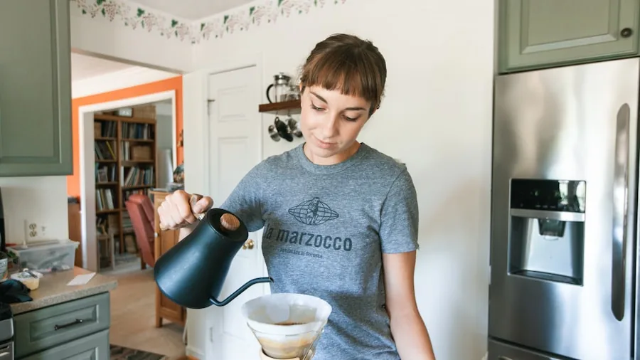 Person pouring hot water over coffee grounds in a bright kitchen during morning routine