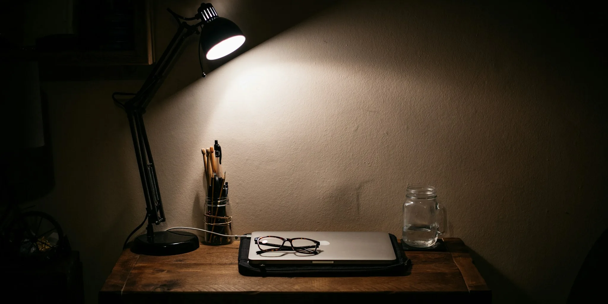 Person reading a book at desk illuminated by warm table lamp in evening light