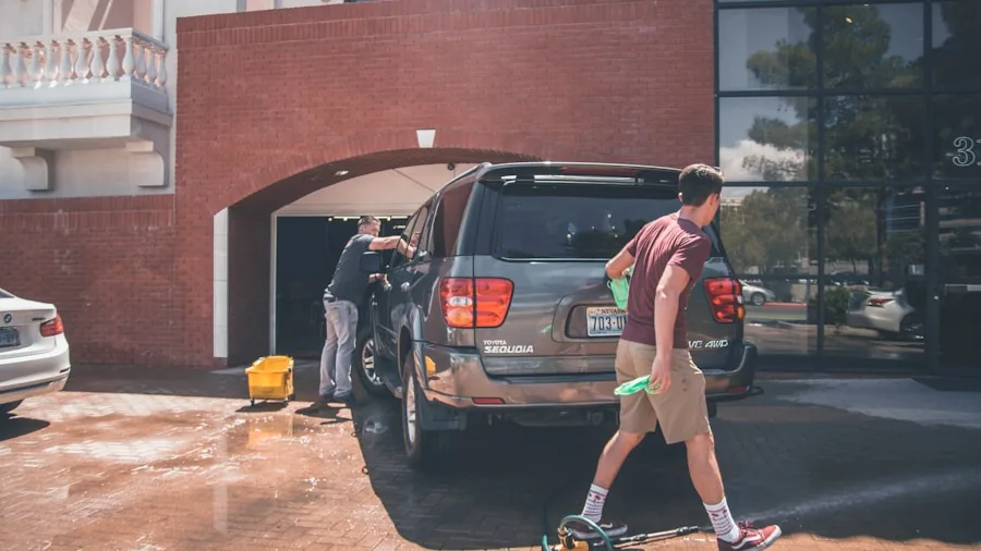 Person rinsing car floor mat with garden hose outdoors on sunny day