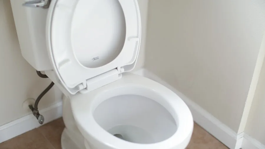 Person using a plunger to unclog a toilet in a home bathroom setting