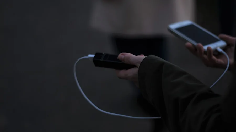 Person using portable battery pack to charge smartphone while traveling outdoors