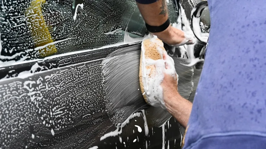 Person using pressure washer equipment to clean car exterior in driveway during daytime