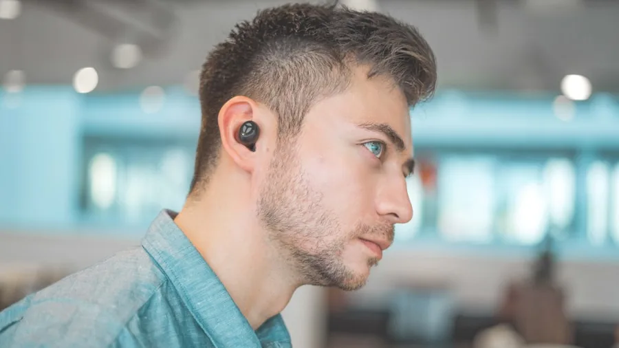 Person wearing earbuds while working on laptop and smartphone, demonstrating multi-device connectivity