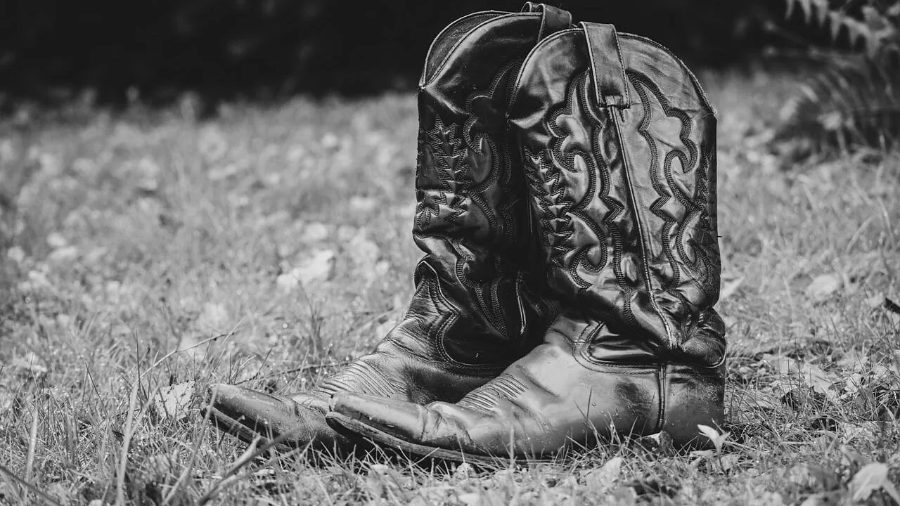 Person wearing western cowboy boots standing outdoors on ranch or rural setting