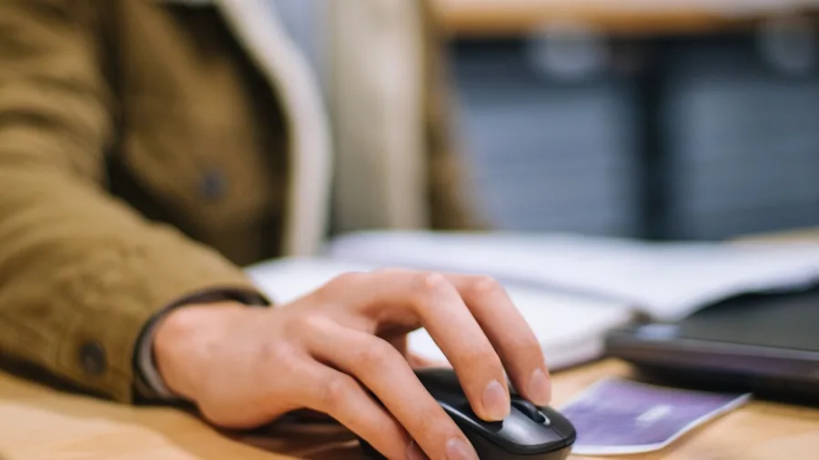 Person working at desk with wireless mouse and laptop in home office setting