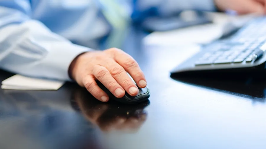Person's hand using ergonomic mouse at wooden desk during work session
