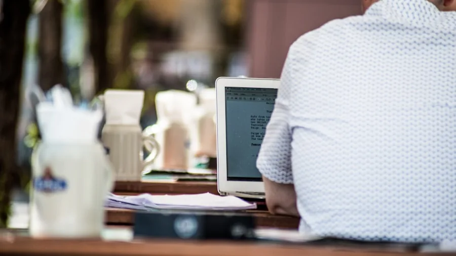 Professional working on laptop at outdoor café during daytime with natural lighting