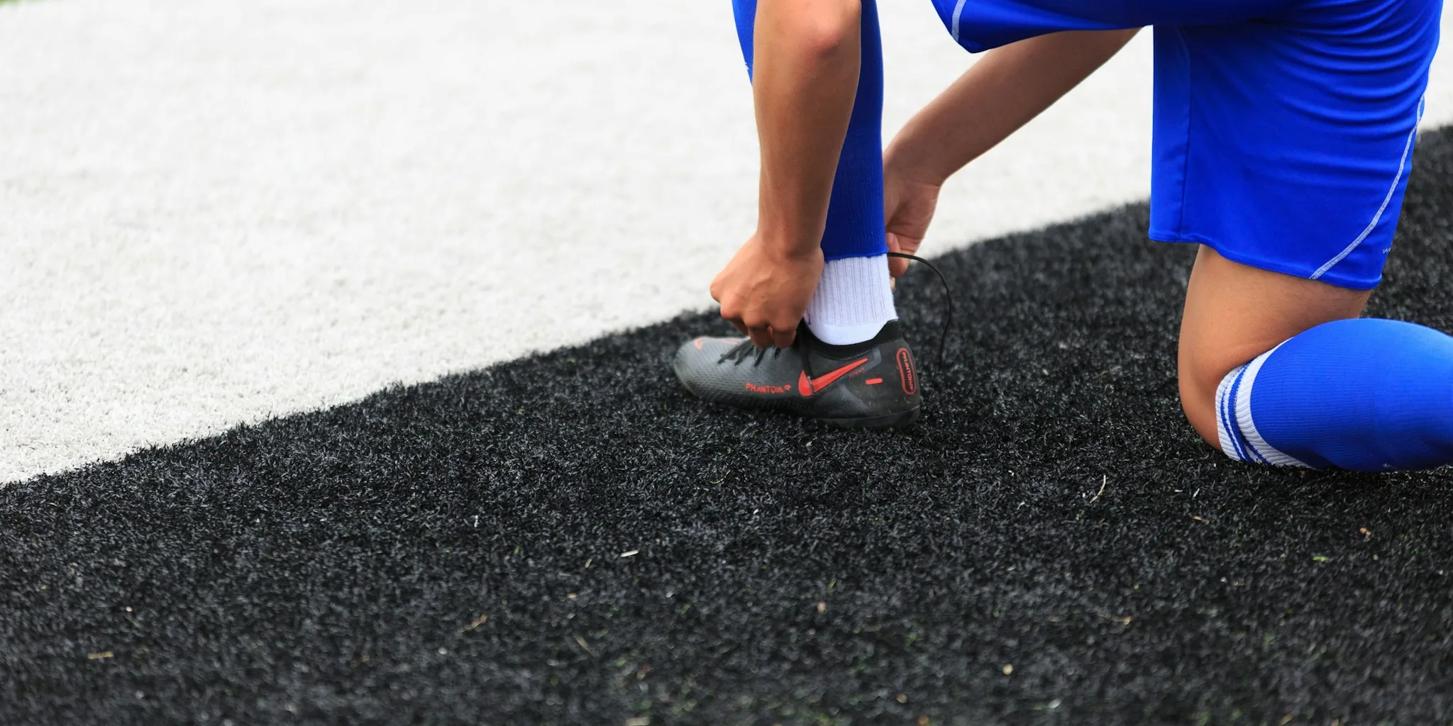Soccer player lacing up cleats on grass field before game