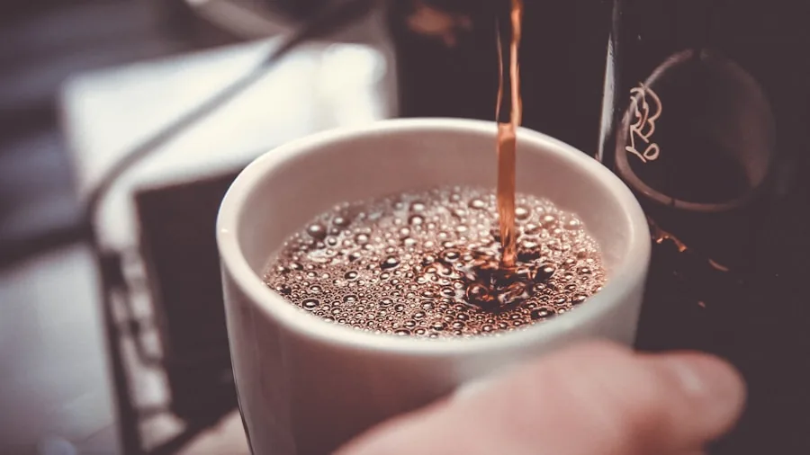 Someone pouring hot water over ground coffee in a filter, morning kitchen light streaming through window