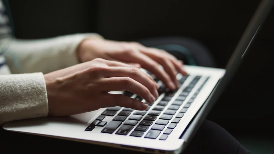 Student typing on laptop keyboard while studying at desk during evening study session