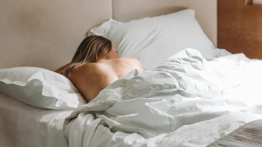 Woman sleeping comfortably on her side in bed with pillows supporting her shoulders and hips