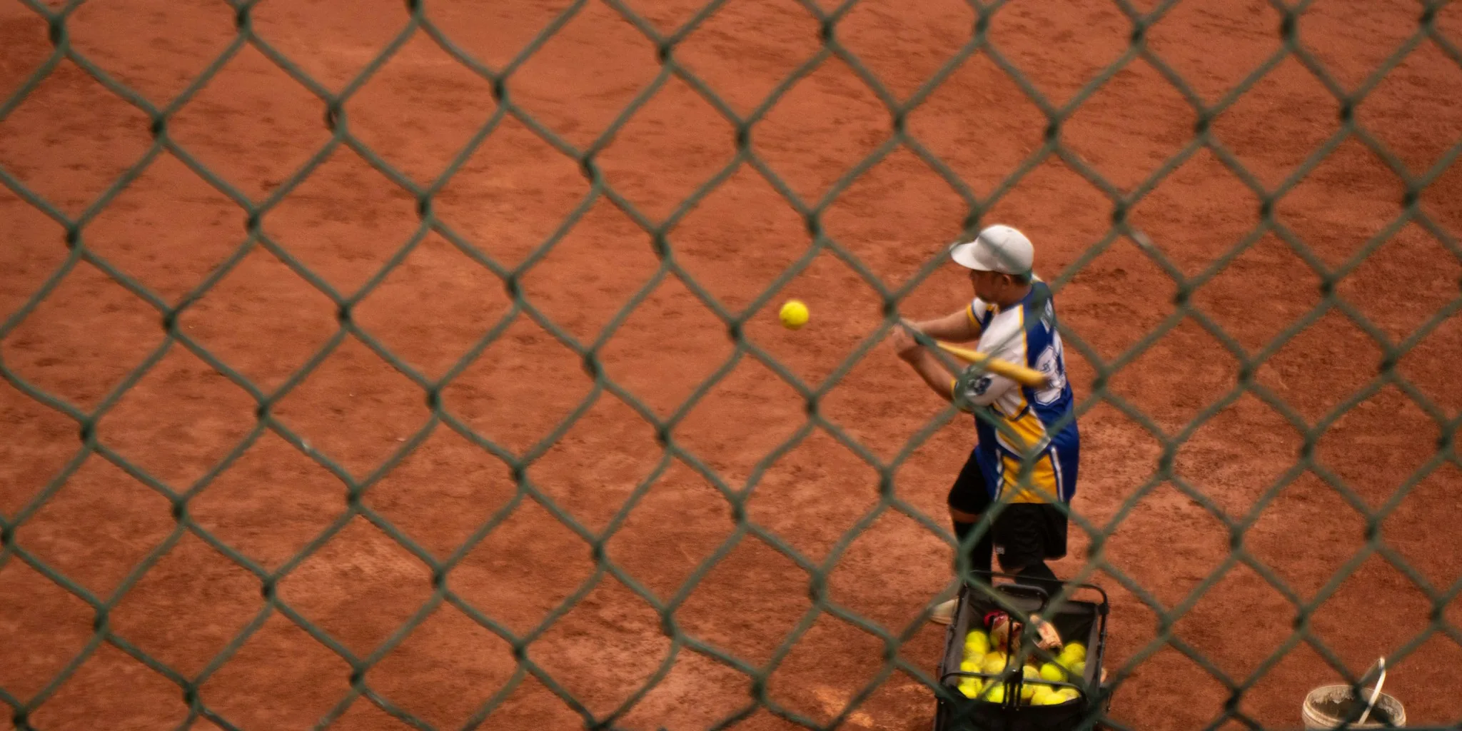 Young woman in softball uniform mid-swing during batting practice on outdoor field